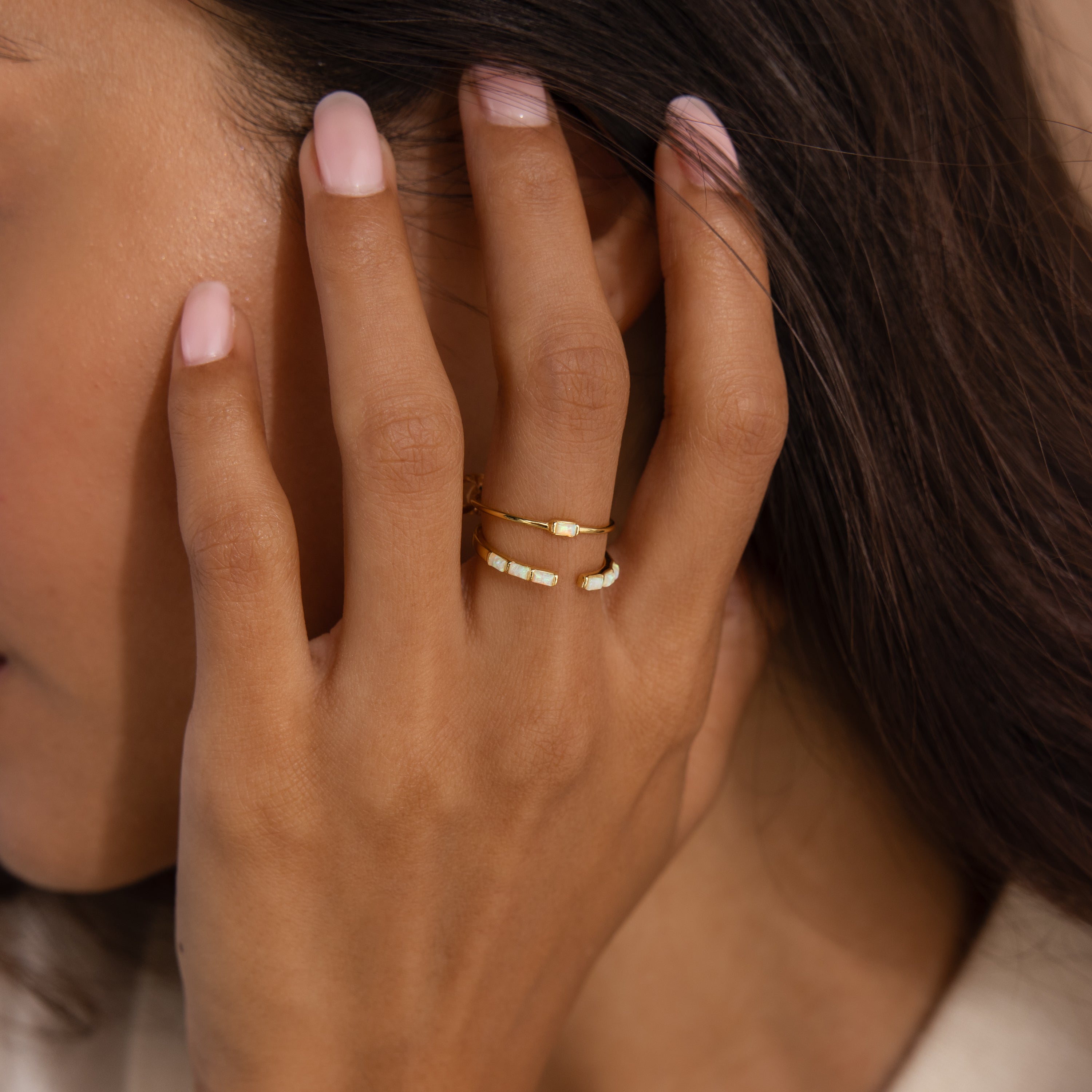 Model wearing a minimalist gold ring set with baguette-cut opals — one with a single opal and the other with five opals in a row.