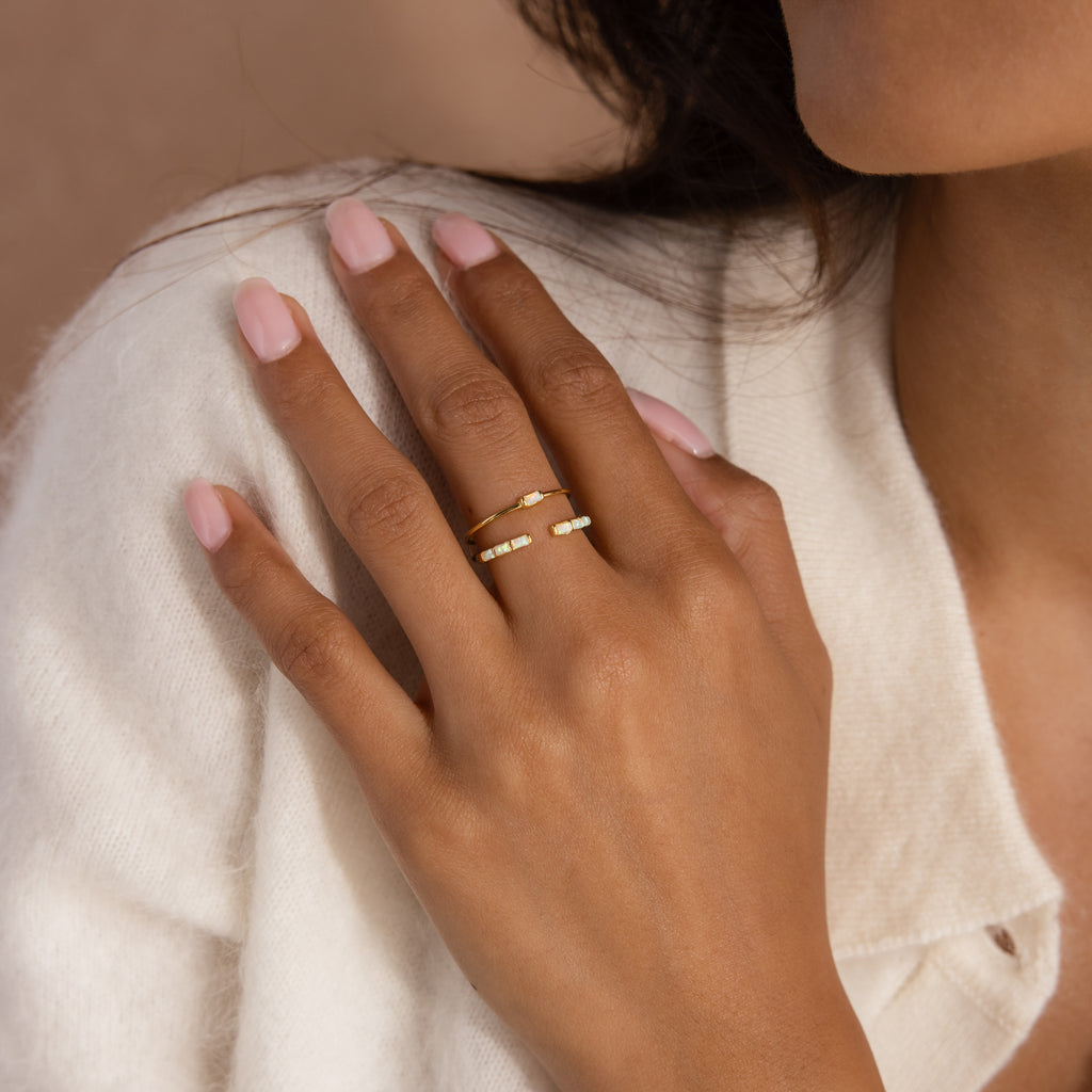 A woman's hand with light pink nails wears the Baguette Opal Ring Set, resting on a cream-colored sweater.