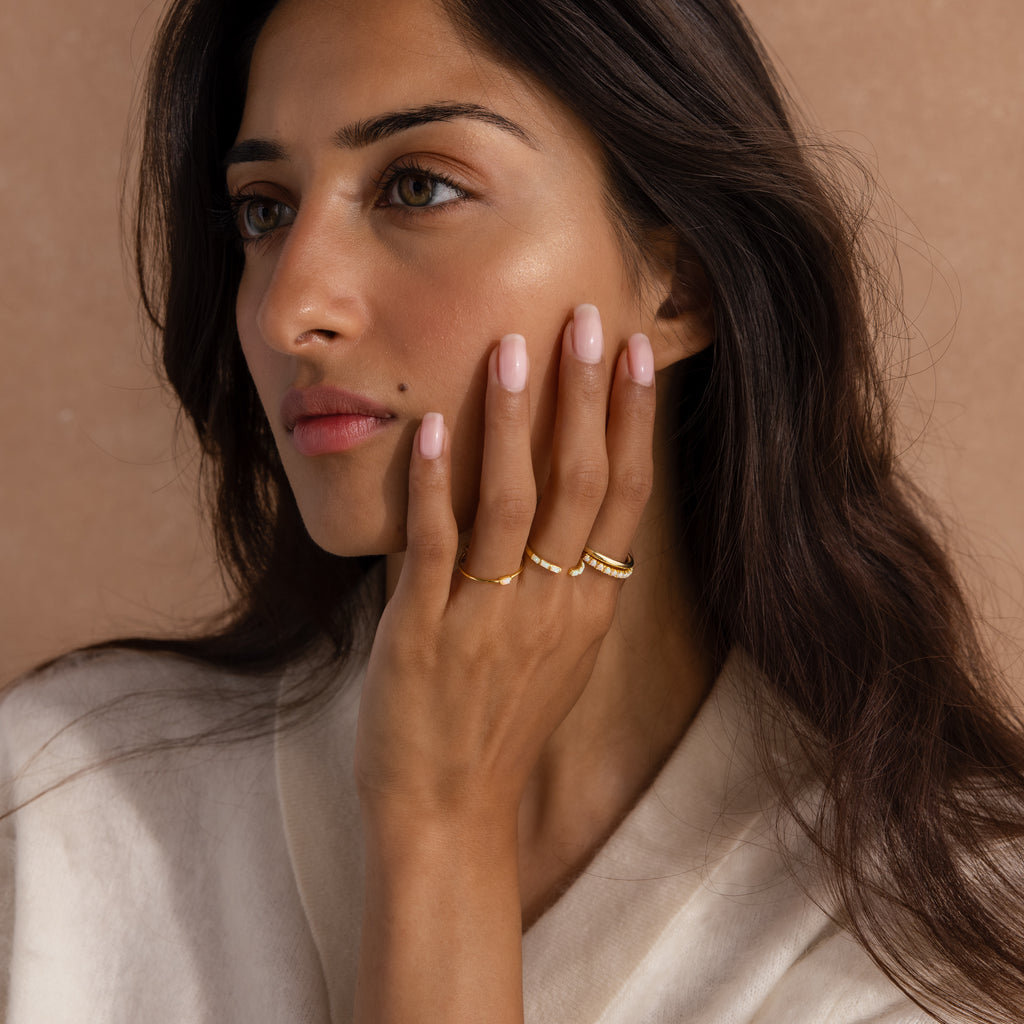 Model wearing multiple dainty gold rings with baguette-cut opals.