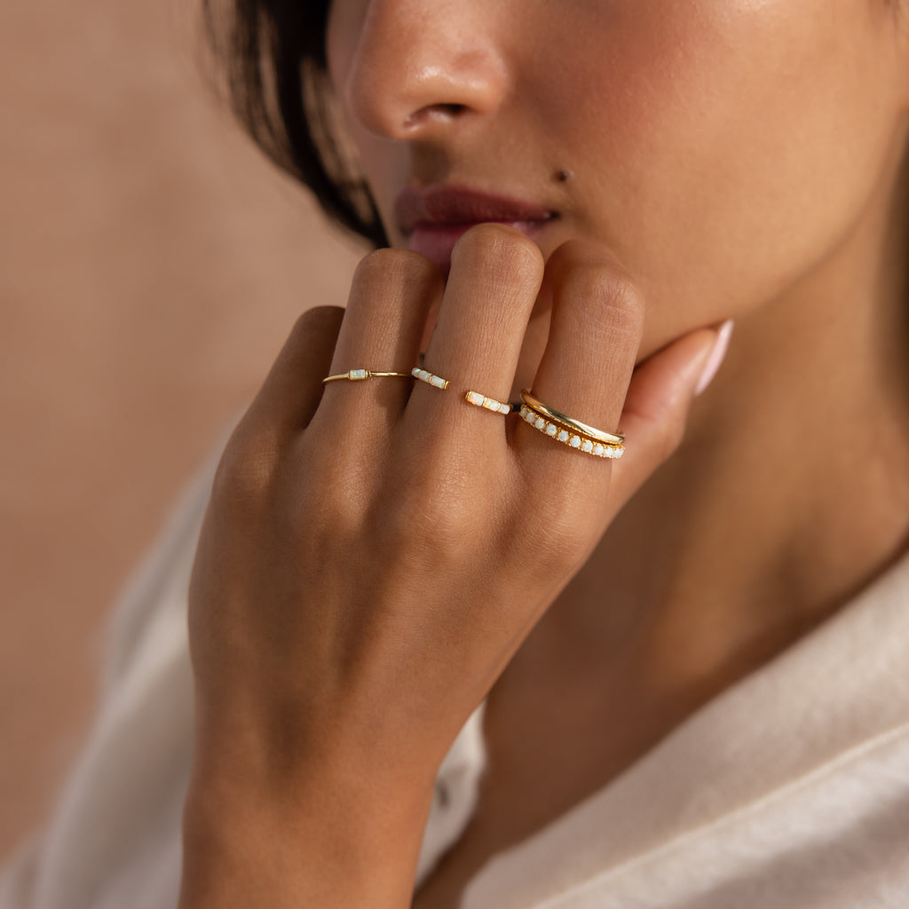 Model wearing a dainty gold opal ring set with baguette-cut stones in varying styles.