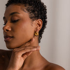 A woman with short curly hair wears Tiger's Eye Duo Hoops and touches her jaw with her hand.