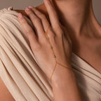 A woman’s hand wearing the Turquoise Hand Chain Bracelet in 18K Gold rests on her shoulder, its delicate design and vibrant stones pairing beautifully with a slim gold bracelet for an elegant layered style.