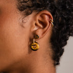 Close-up of a person with curly hair wearing gold hoop earrings and a gold ear cuff, featuring the Tiger's Eye Duo Hoops for an elegant and sophisticated touch.