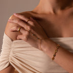 A woman wears a Turquoise Hand Chain Bracelet in 18K Gold paired with gold rings and a delicate chain bracelet against a beige, off-shoulder top.