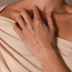 A woman wears the Turquoise Hand Chain Bracelet with blue beads over beige, off-shoulder fabric.