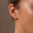 Closeup of a womans ear wearing Floating Blue Zircon Huggies against a blurred brown background.