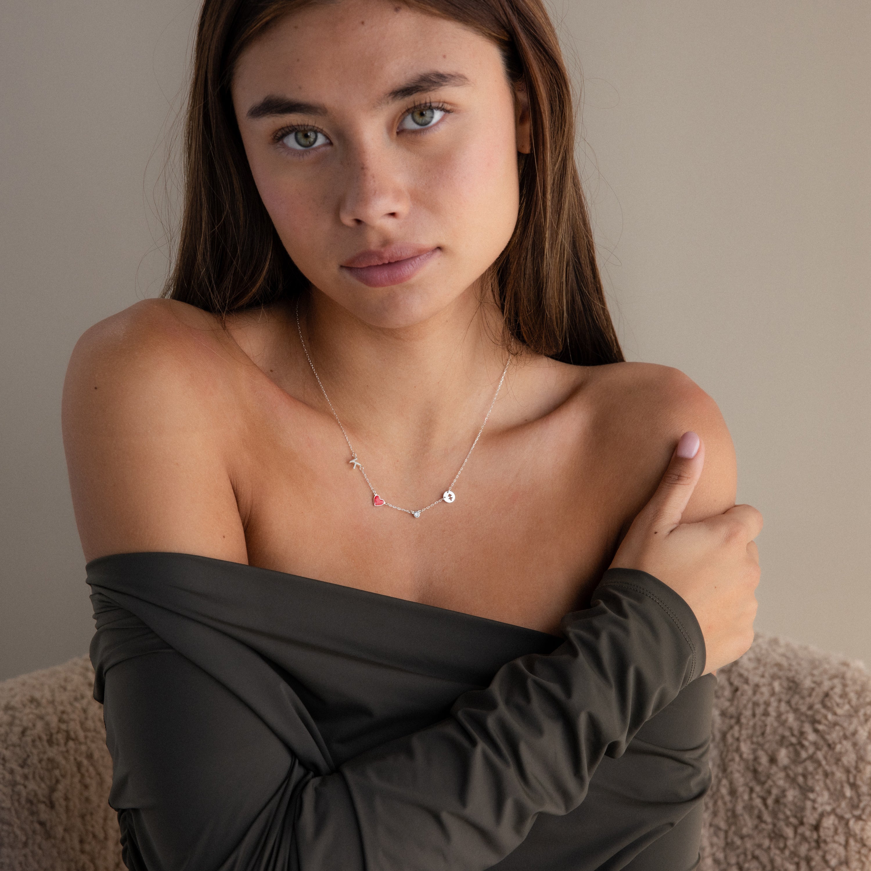 A woman with long brown hair, wearing an off-shoulder top and the Dainty Space Charm Necklace in Sterling Silver, gazes softly at the camera.
