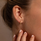Close-up of a womans ear wearing Floating Topaz Huggies, her hand touching her neck and showcasing elegant personalized gold hoop earrings.