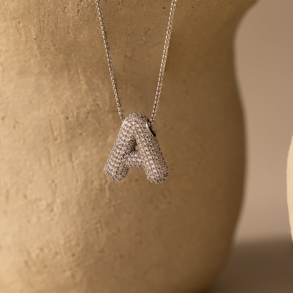 Pave Puff Letter Necklace in White Gold pendant displayed against a beige textured background.