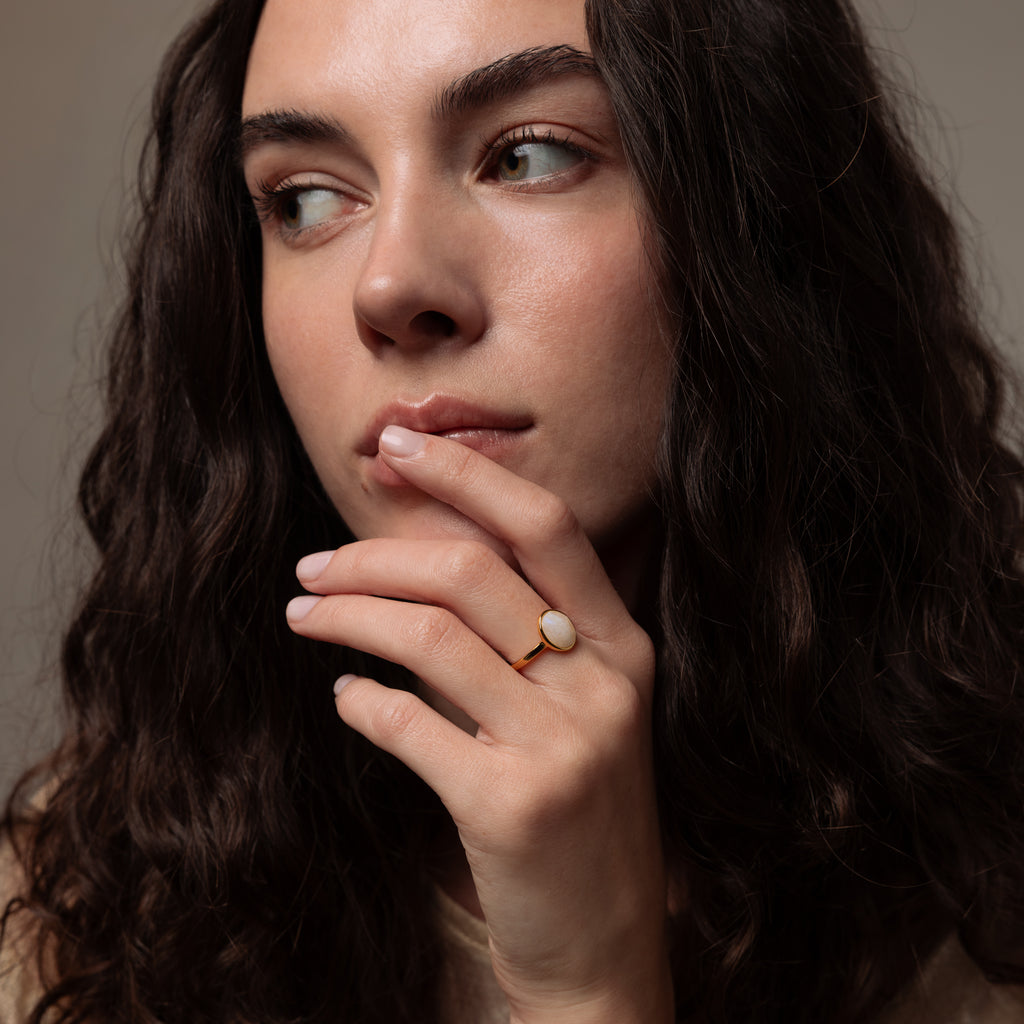Woman with long brown hair gazes sideways, resting her hand near her lips, showing off the Moonstone Signet Ring.