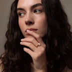 Woman with long brown hair gazes sideways, resting her hand near her lips, showing off the Moonstone Signet Ring.