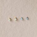 Four pairs of Raindrop Opal Studs featuring opal and diamond accents in gold and silver settings, displayed on a beige textured background—ideal as birthstone or classic earrings.