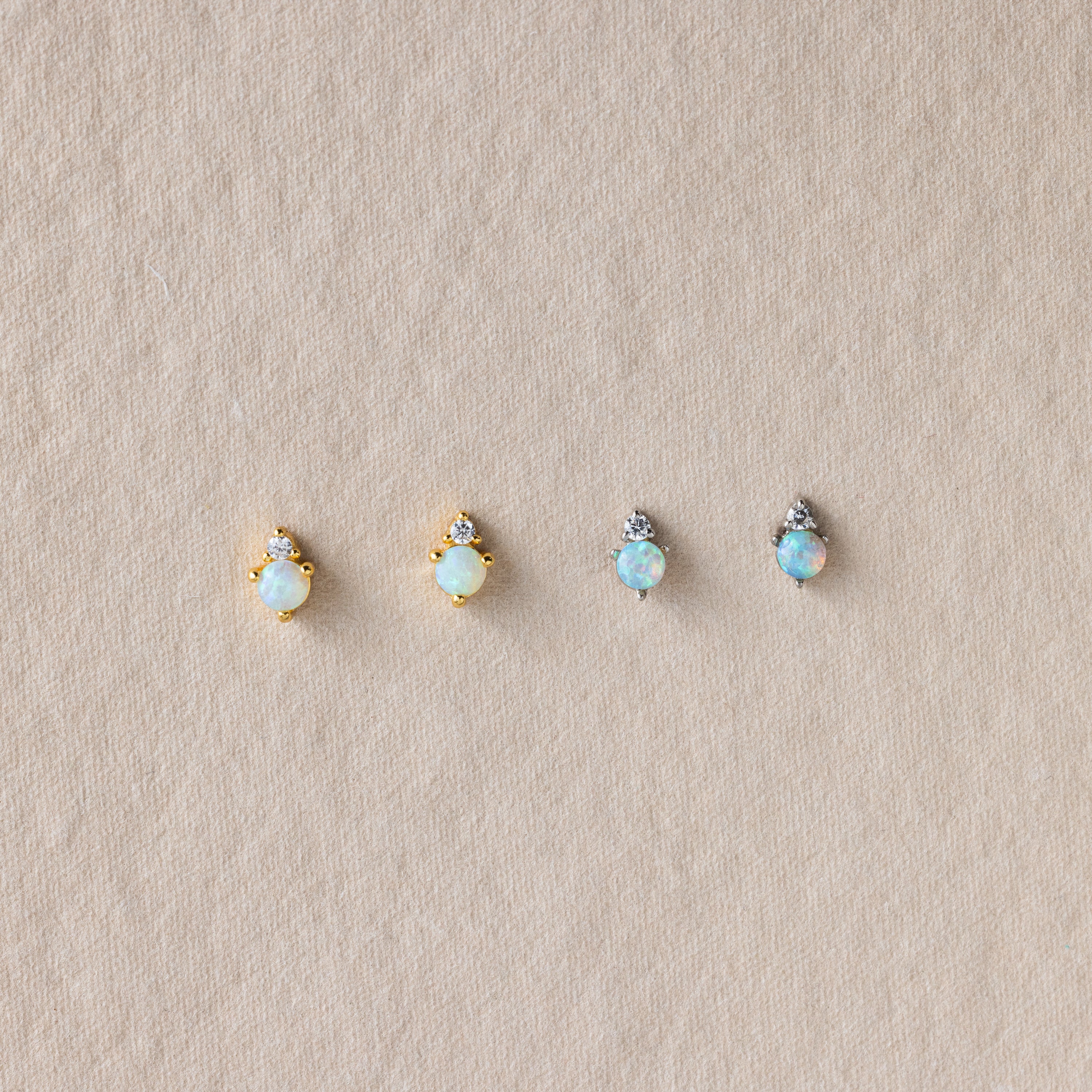 Four pairs of Raindrop Opal Studs featuring opal and diamond accents in gold and silver settings, displayed on a beige textured background—ideal as birthstone or classic earrings.