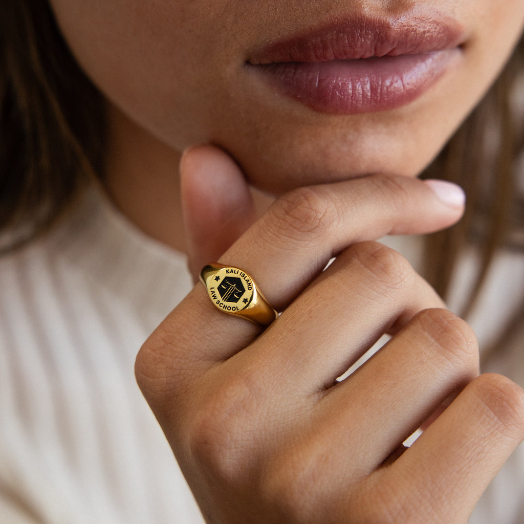 A person wearing the College Emblem Signet Ring—an ideal graduation gift—rests their hand on their chin, lips slightly parted.