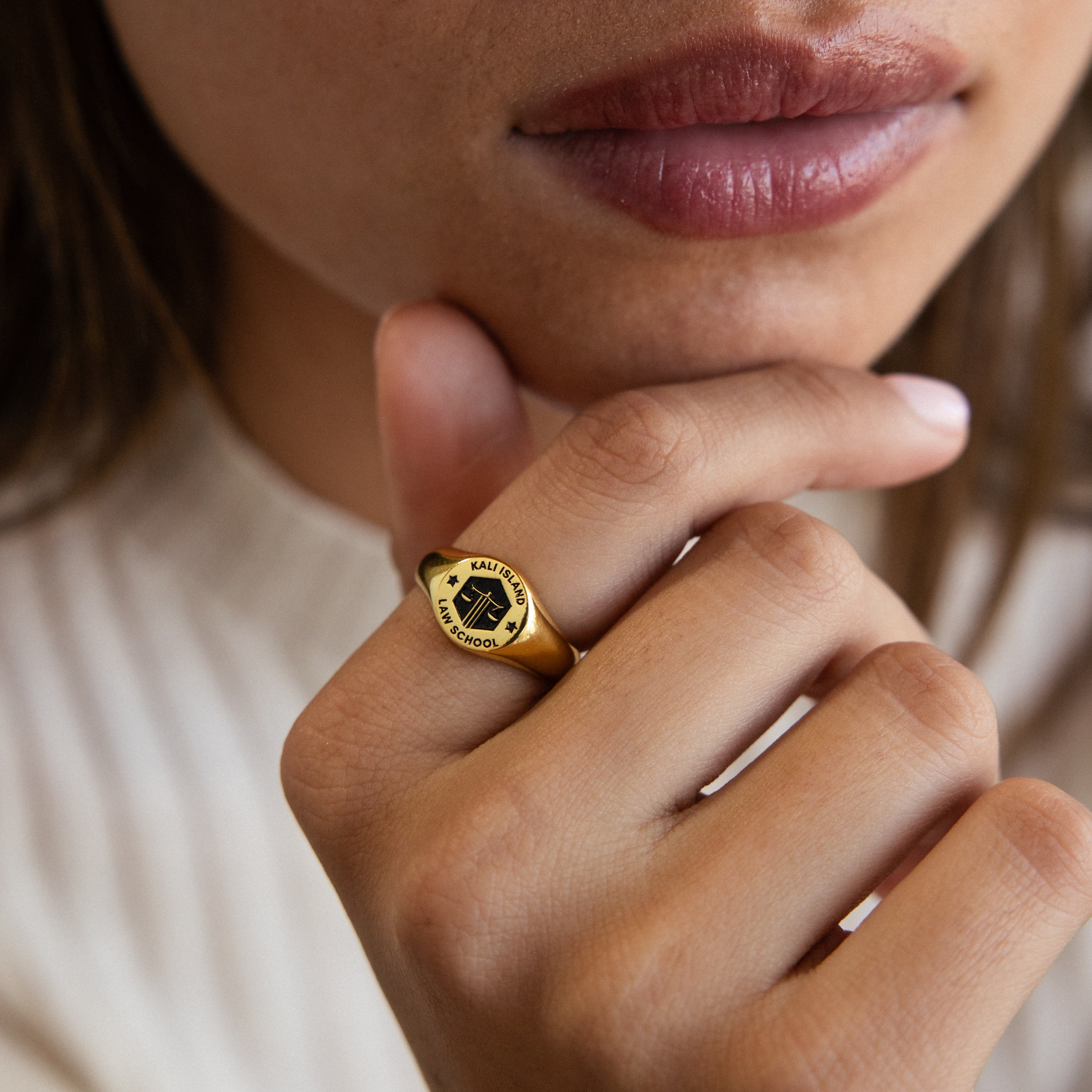 A person wearing the College Emblem Signet Ring—an ideal graduation gift—rests their hand on their chin, lips slightly parted.