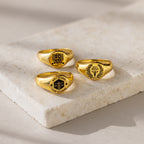 Three College Emblem Signet Rings with engraved law school emblems are displayed on a light stone surface—an ideal graduation gift to celebrate achievement.