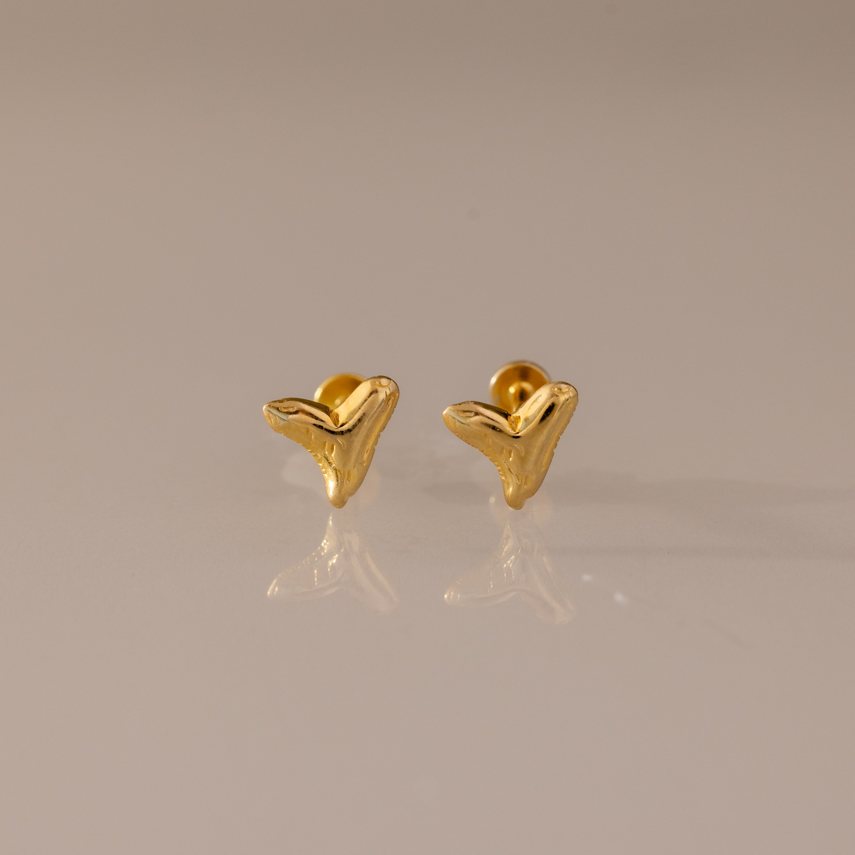 Shark Tooth Flatback Studs in 18K Gold are small, abstract chevron-shaped earrings—perfect as a summer jewelry choice, shown here on a neutral reflective surface.