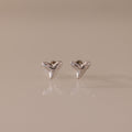 Pair of small, silver Shark Tooth Flatback Studs on a reflective light beige surface—an elegant beach accessory perfect for ocean lovers.