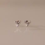 Pair of small, silver Shark Tooth Flatback Studs on a reflective light beige surface—an elegant beach accessory perfect for ocean lovers.