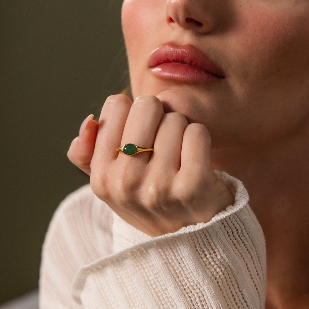 A woman rests her chin on her hand in soft natural light, showcasing the elegant Oval Jade Signet Ring.