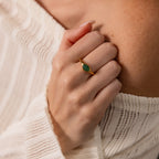 A hand wearing the Oval Jade Signet Ring with a vibrant green jade stone set in gold and a white off-shoulder knit sweater.