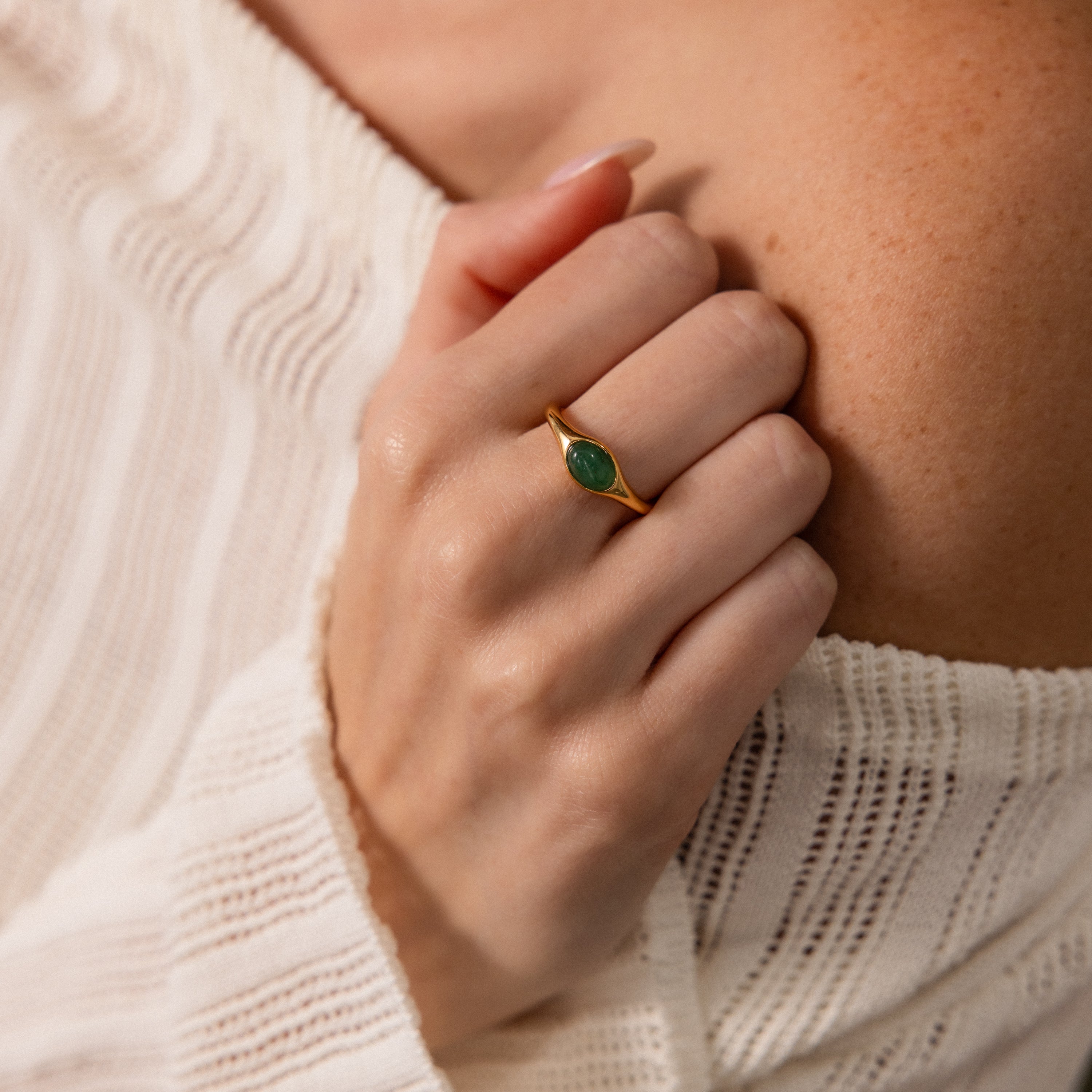 A hand wearing the Oval Jade Signet Ring with a vibrant green jade stone set in gold and a white off-shoulder knit sweater.