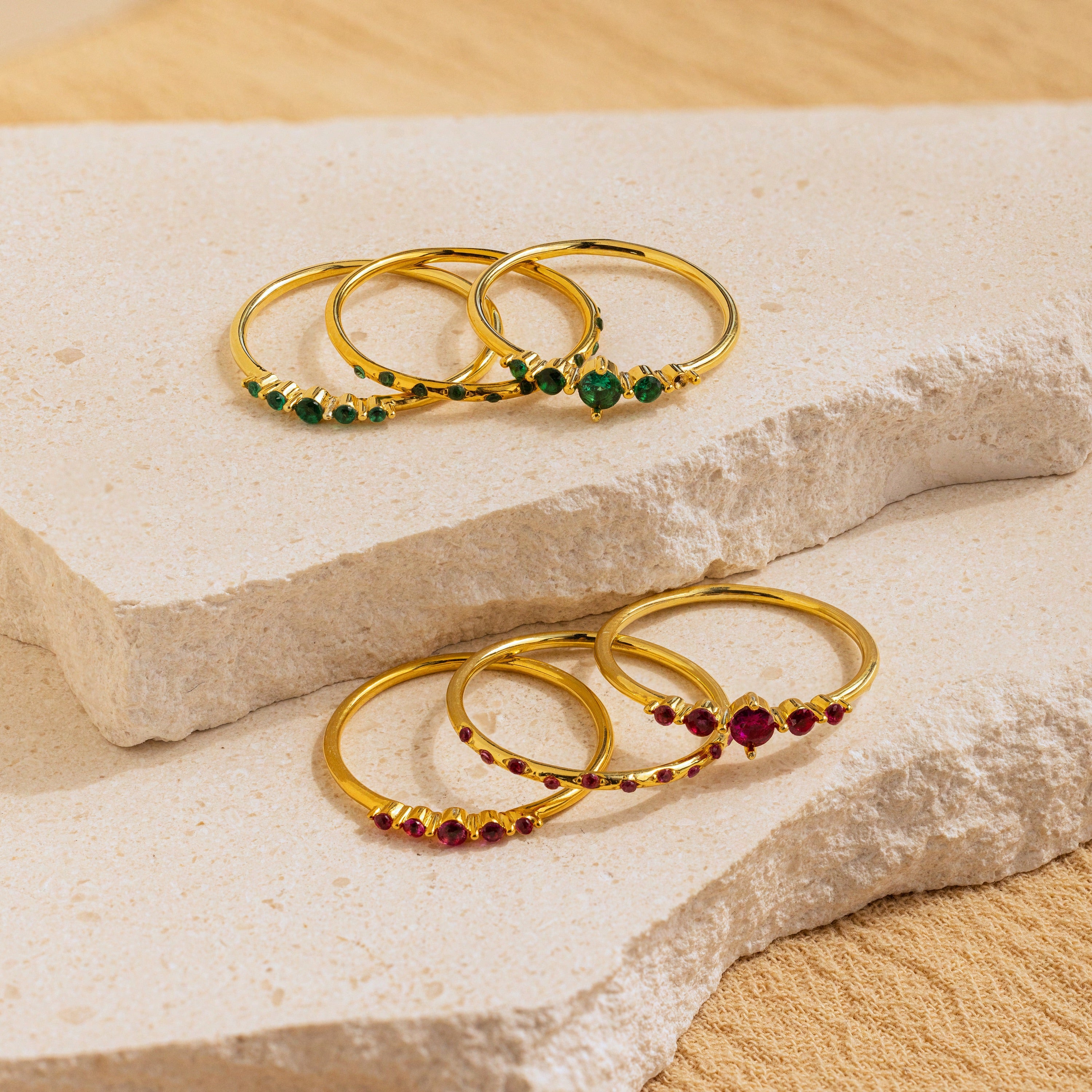 Six Lace Birthstone Rings from the Lace Birthstone Rings Set, each with a vibrant gemstone, are arranged on beige stone slabs in natural light—a beautiful minimalist collection and a perfect personalized gift.