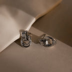 Micro Triple Knot Earrings in Silver displayed on a neutral background with soft shadows and highlights, evoking a sense of quiet luxury.
