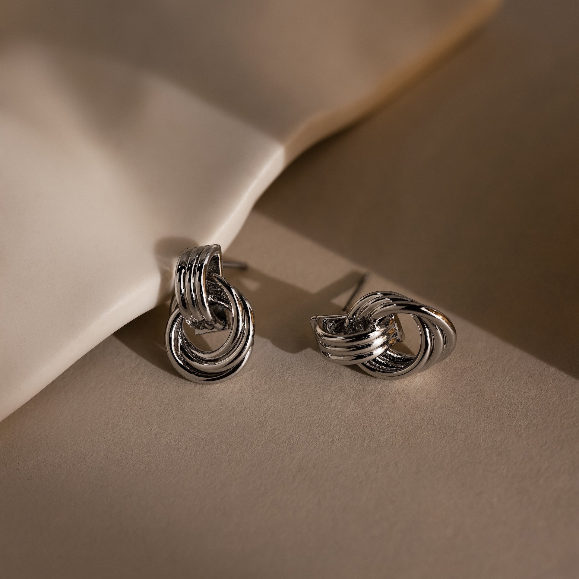 Micro Triple Knot Earrings in Silver displayed on a neutral background with soft shadows and highlights, evoking a sense of quiet luxury.