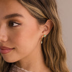 Woman with long wavy hair wearing Jade Marquise Huggies in 18K Gold, looking to the side.