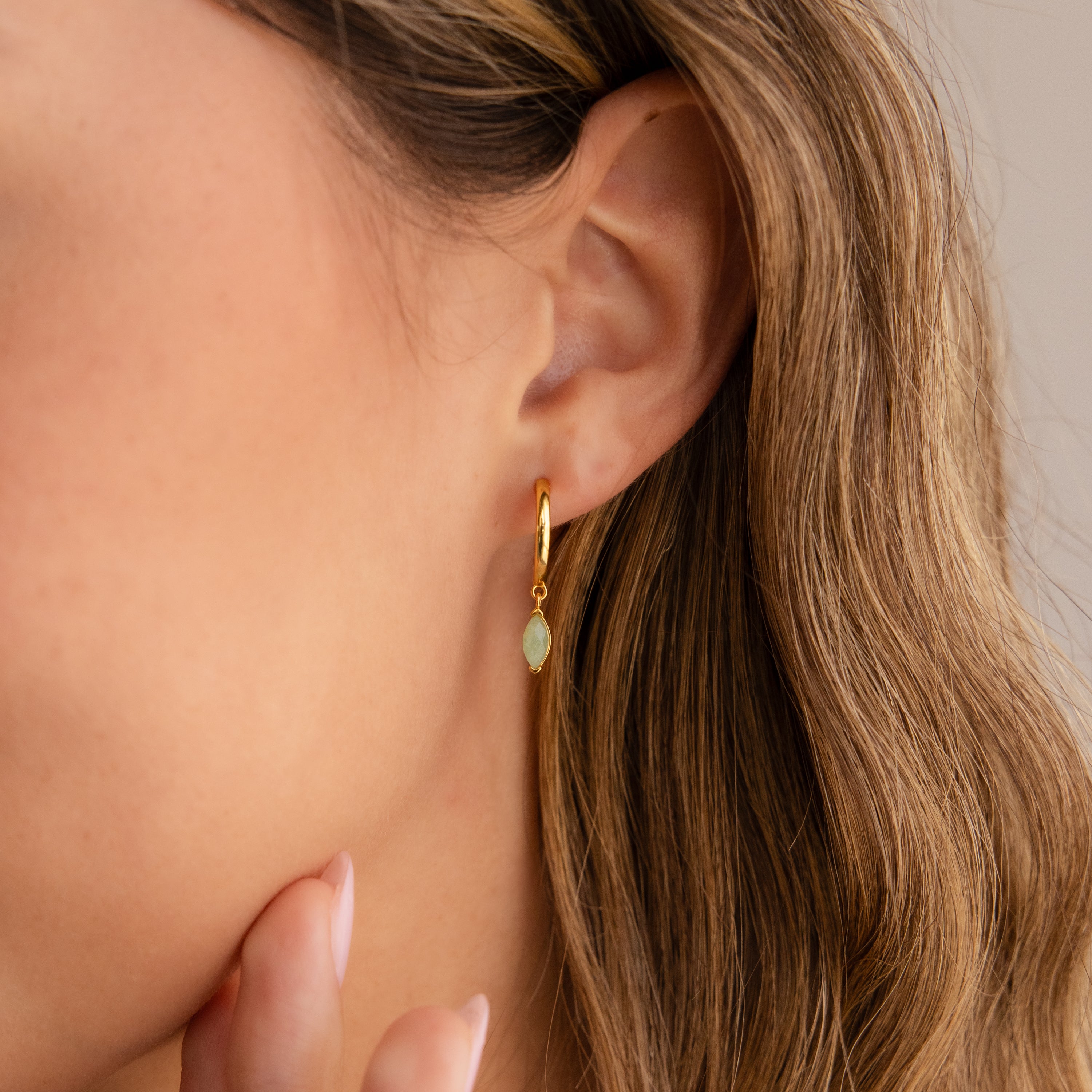 Close-up of a womans ear wearing Jade Marquise Huggies with a light green stone, as her hand gently touches her chin.
