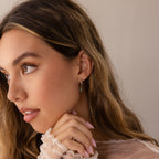 Woman with long hair wearing a sheer top and Jade Marquise Huggies, gazing left with her hand near her face.