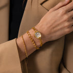 A person wearing the Heirloom Chain Link Timepiece and two gold bracelets, dressed in a tan blazer and black top.