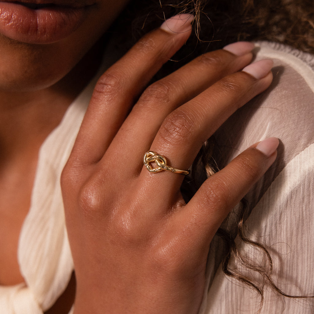 A hand with manicured nails wears the Starry Love Knot Ring, resting gently on the chest near the face.