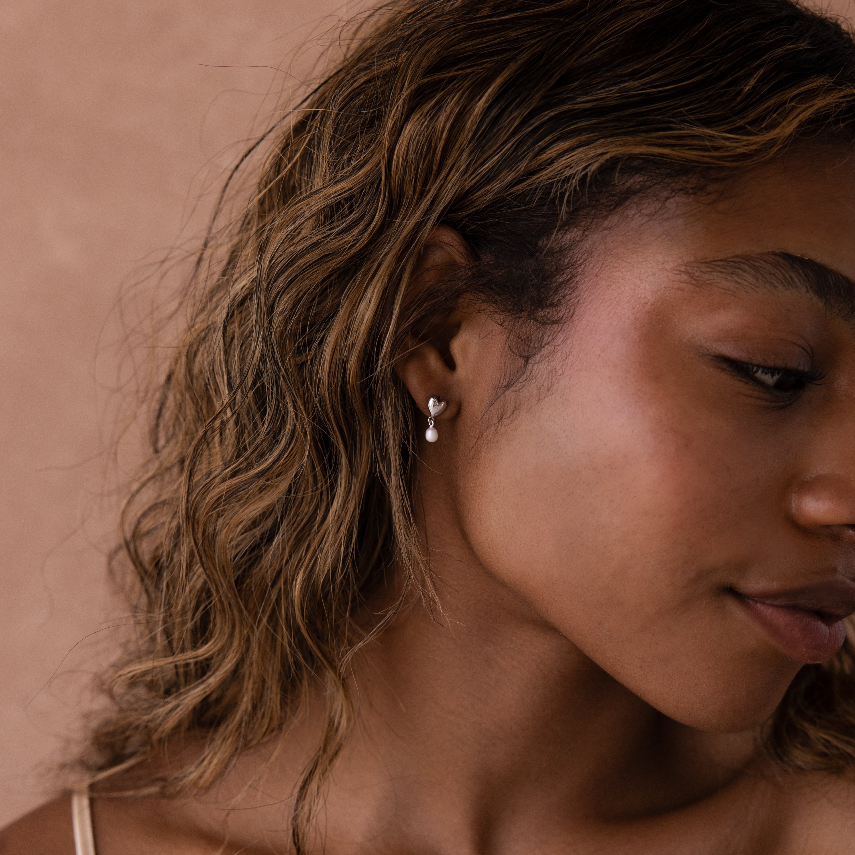 Close-up of a woman with wavy hair facing slightly right, wearing Heart Pearl Drop Earrings.