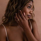 A woman with wavy hair gently touches her face, wearing the Pave Double Knot Ring in soft natural lighting.