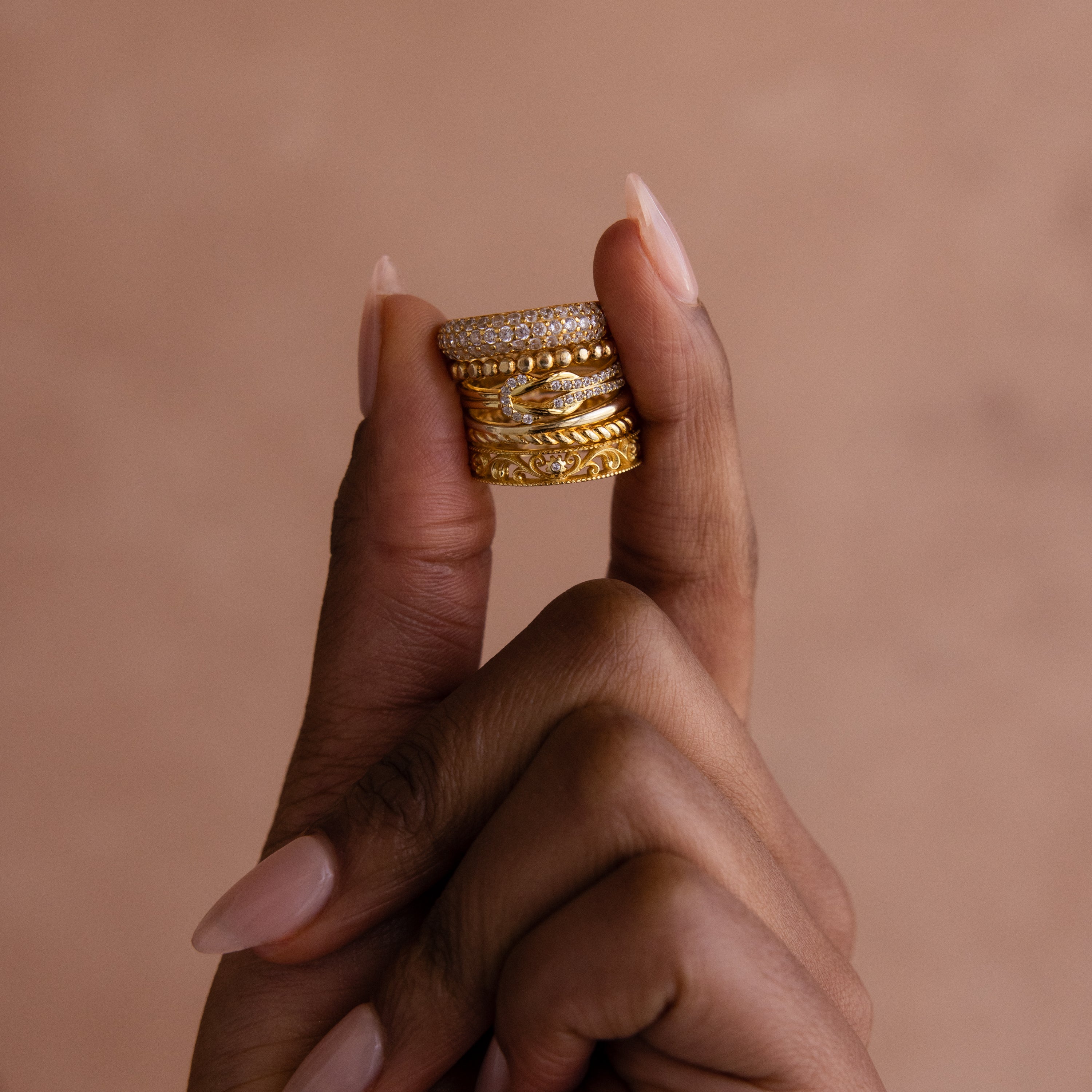 A hand holds the Pave Double Knot Ring—stacked gold rings featuring sparkling stones—set against a beige background.