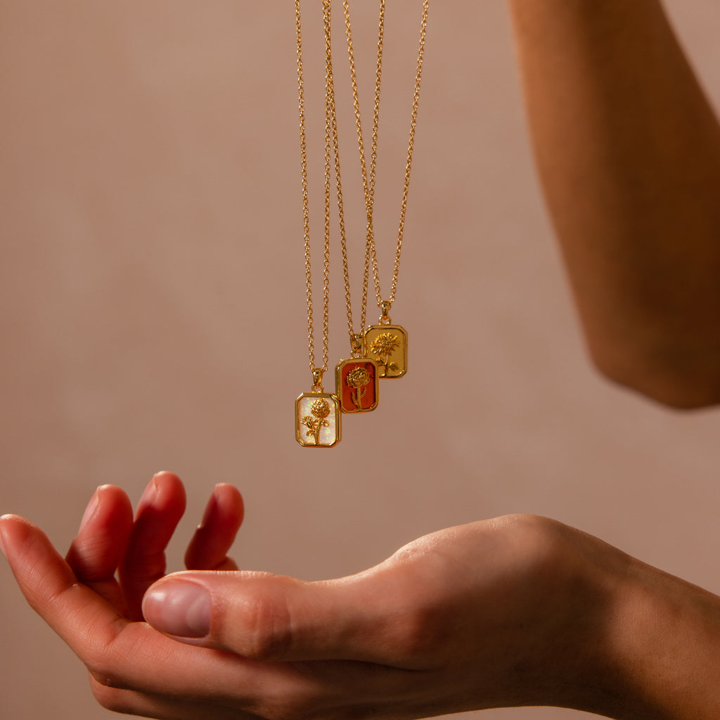 The Opal Birth Flower Charm Necklace features a delicate engraved gold pendant, elegantly showcased above an open hand against a neutral background—ideal for those seeking refined, timeless jewelry.