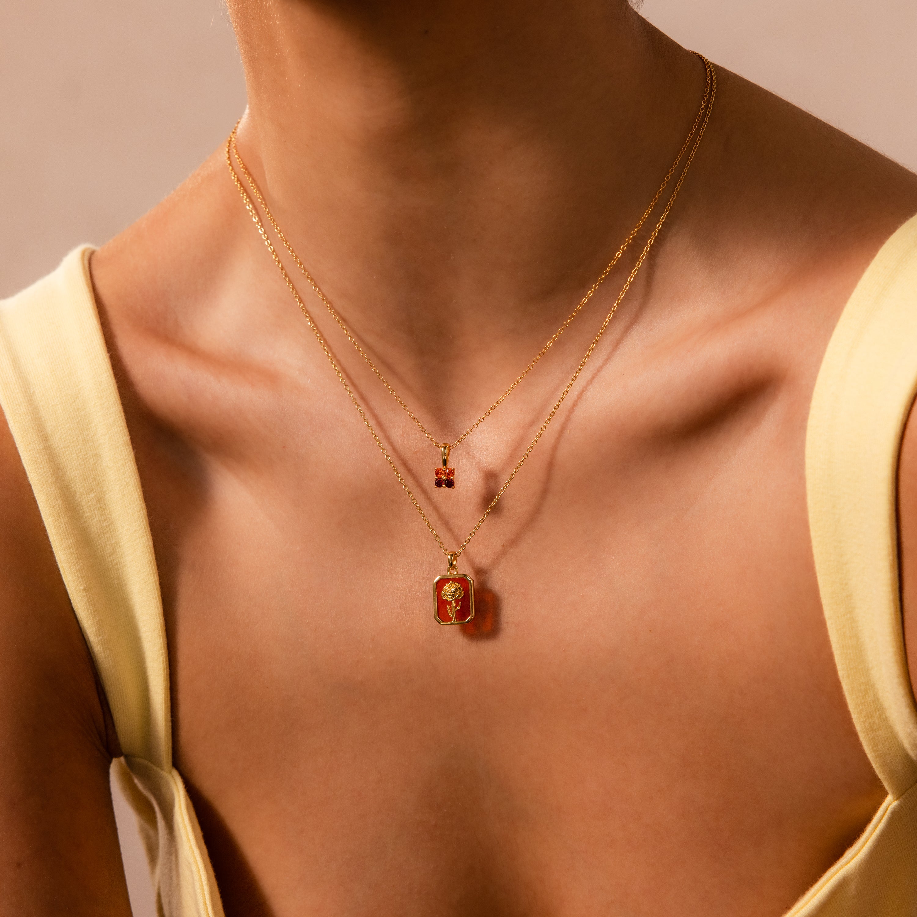 Close-up of a woman wearing the Alexandrite Birth Flower Charm Necklace layered with gold chains, paired with a yellow sleeveless top—perfect for adding vibrant elegance to your jewelry collection.