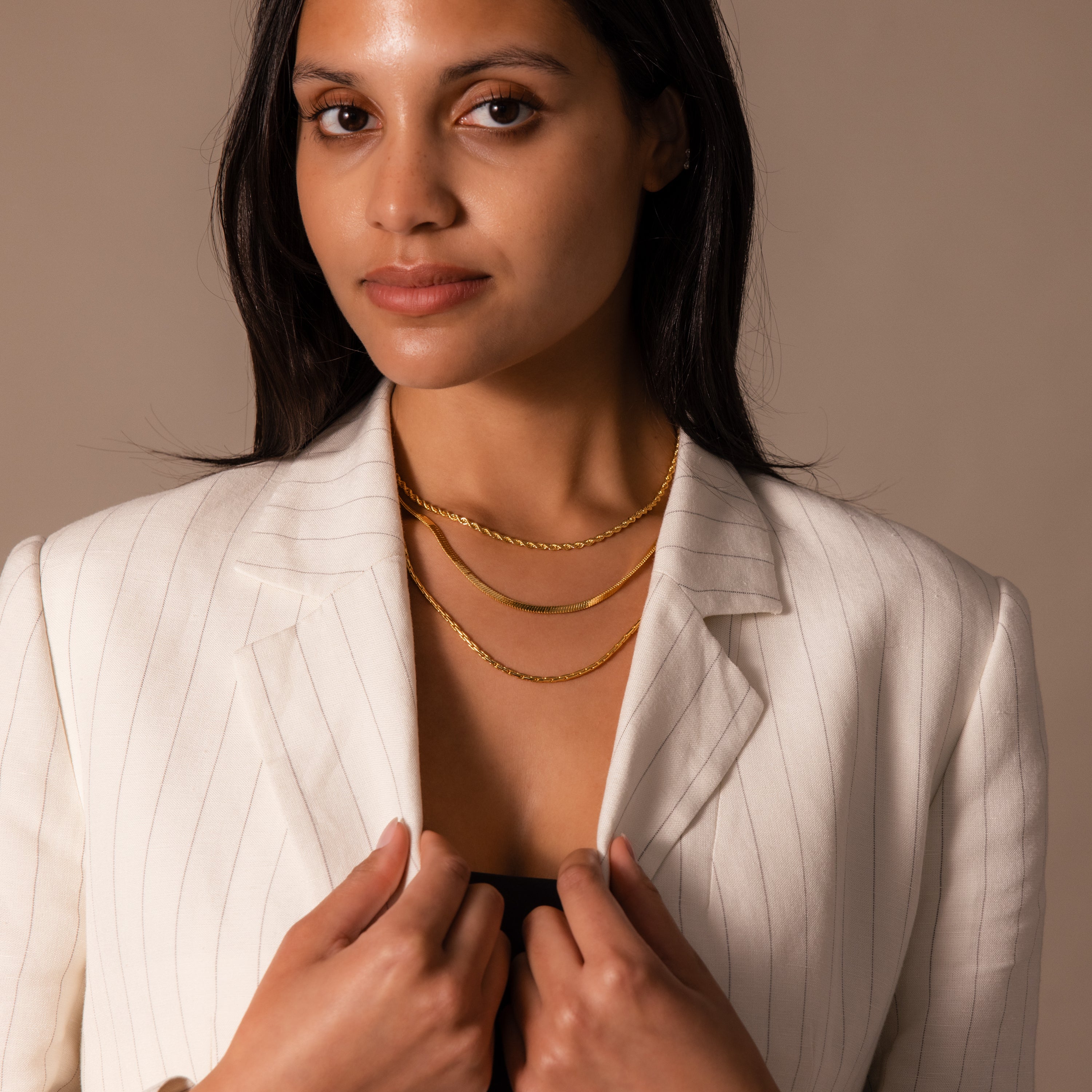 Woman in a white pinstripe blazer faces the camera with a neutral expression, wearing the Bold Link Chain Necklace layered over her outfit.