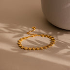 The Ribbed Heart Link Bracelet is laid flat on a matte beige surface, with soft, natural light casting delicate shadows