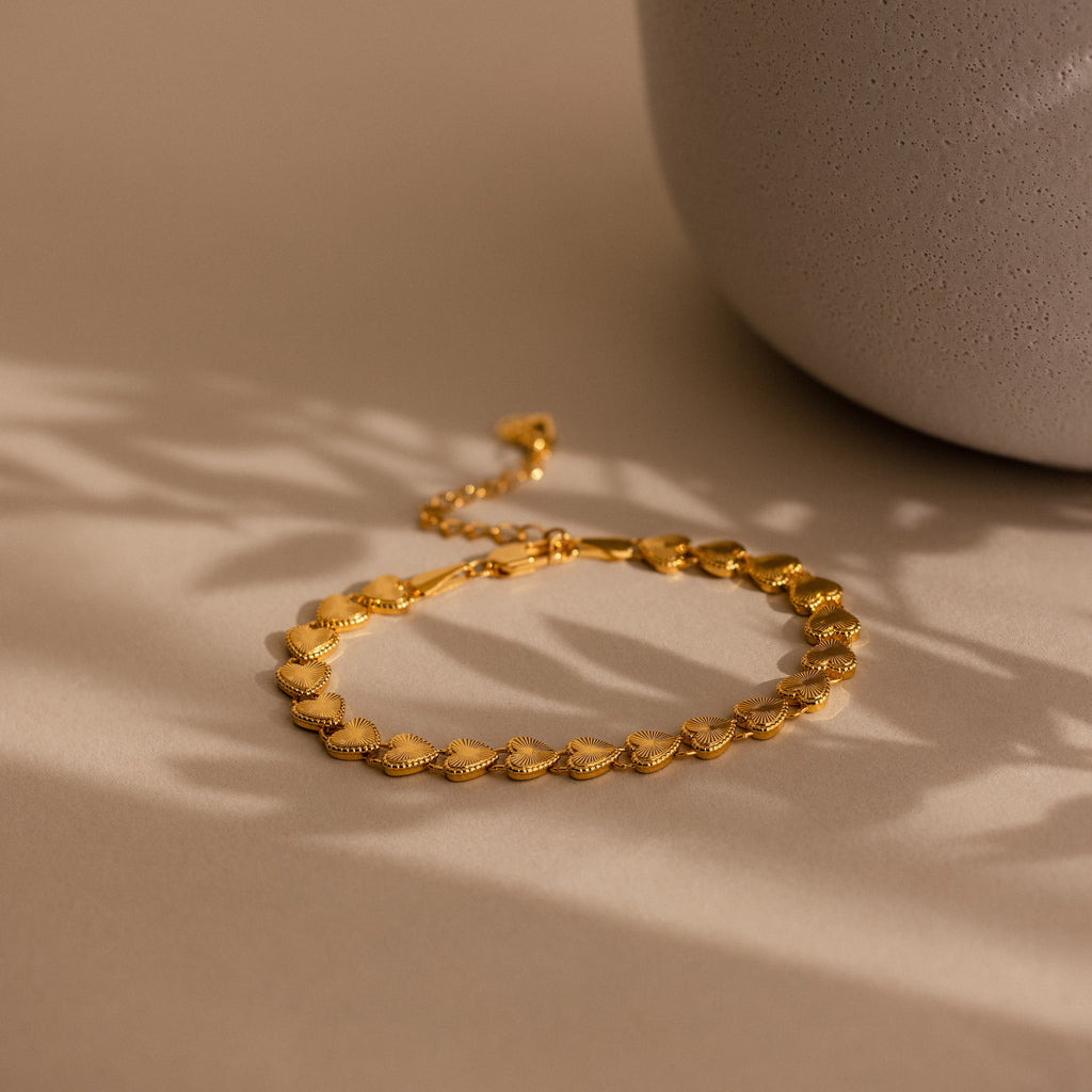 The bracelet laid flat on a neutral beige surface next to a ceramic vase, with soft shadows cast across it.