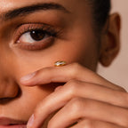 A woman holds the Pave Dome Charm in 18K Gold near her face, its sparkling design catching the light and highlighting her eye with graceful elegance.