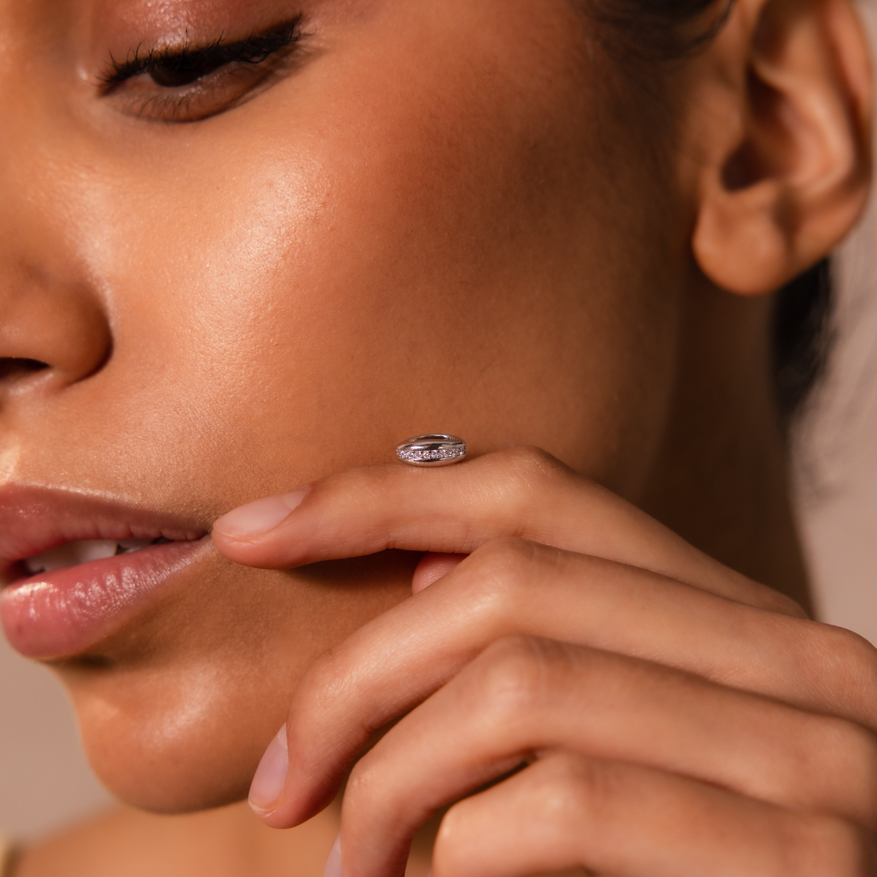 A woman’s face in profile with her hand near her lips, showcasing the Pave Dome Charm in Silver, a ring that adds a touch of sparkle.