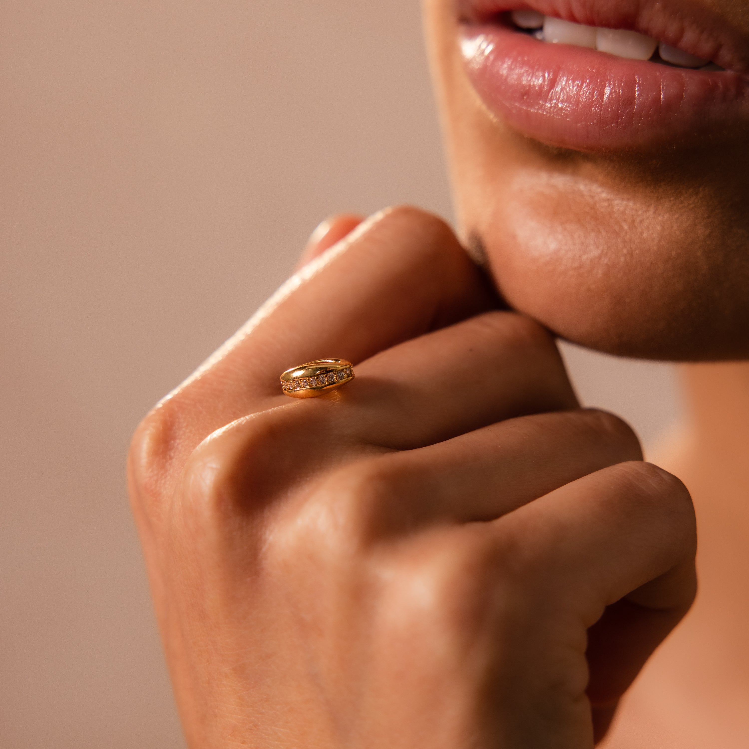 With parted lips and a hand near their face, a person showcases the Pave Dome Charm—a gold ring with small stones that's perfect for charm stacks or anyone who loves delicate, elegant jewelry.