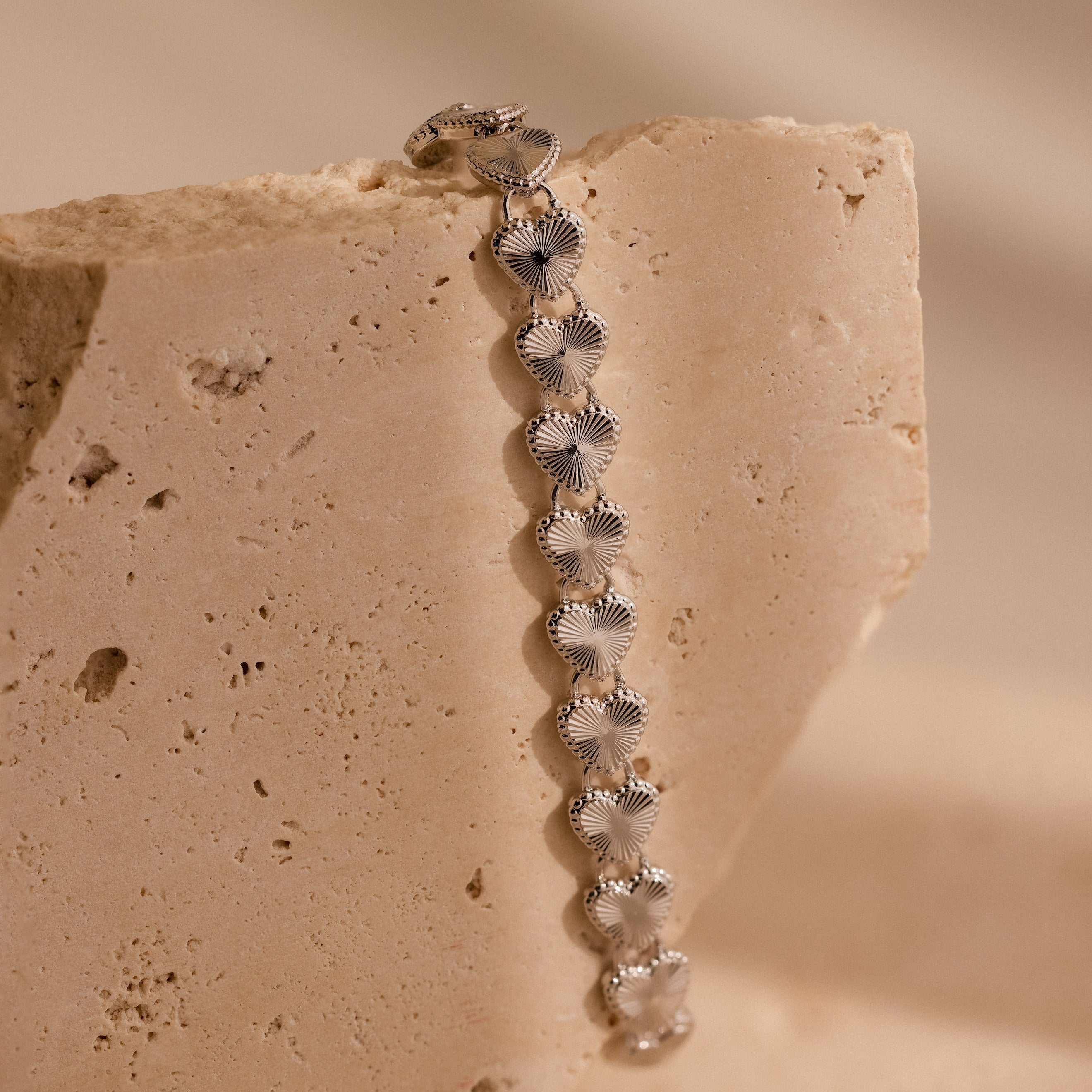 A vertical close-up of the Ribbed Heart Link Bracelet in White Gold draped over a textured stone surface.