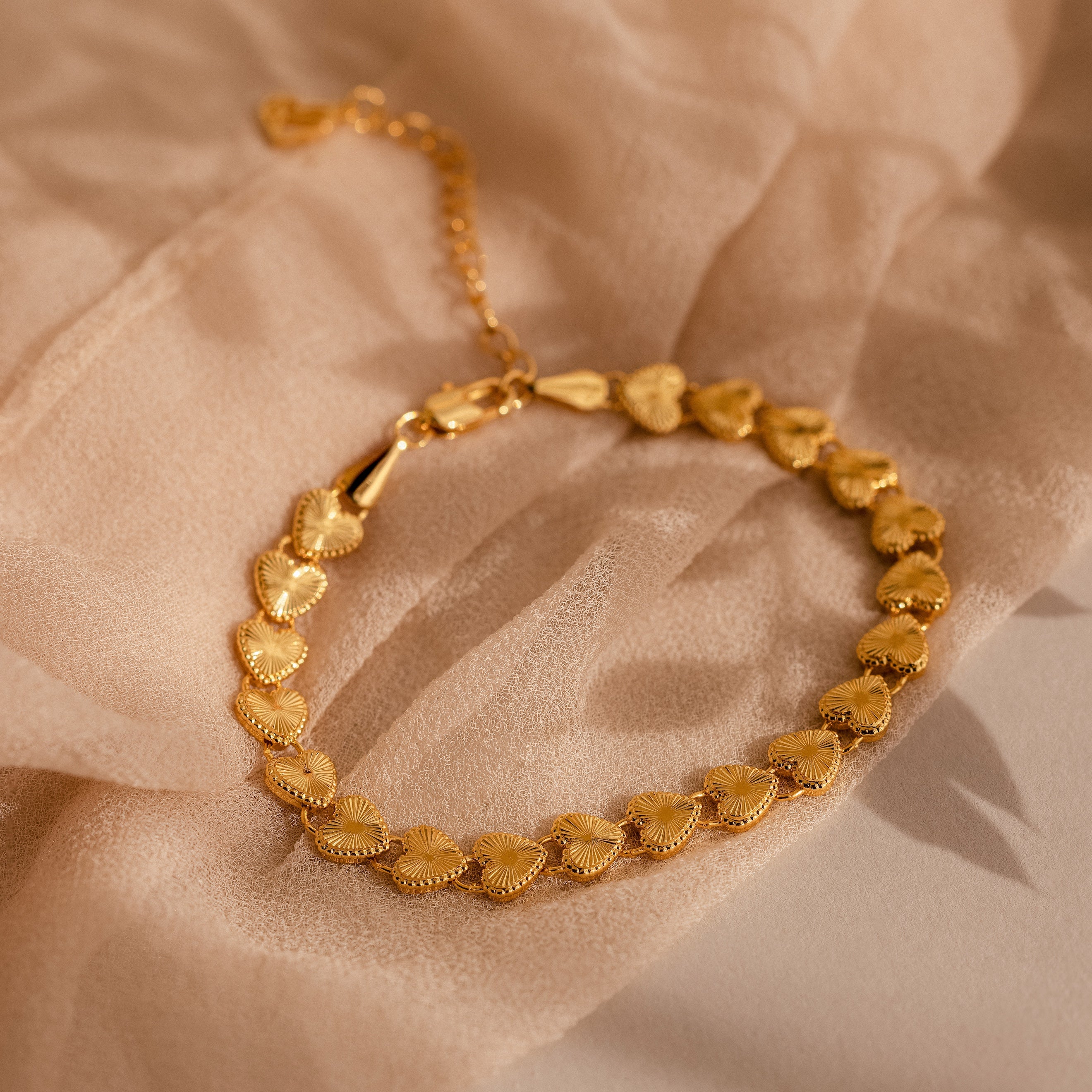 Close-up of the bracelet resting on light, sheer beige fabric, showcasing its textured heart details.