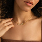 Woman wearing the Pave Dream Script Name Necklace in gold, personalized with "Natalie," delicately holding the chain near her collarbone.