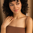 A woman in a brown top smiles and looks to the side while wearing the Pave Dream Script Name Necklace in gold, personalized with "Natalie.
