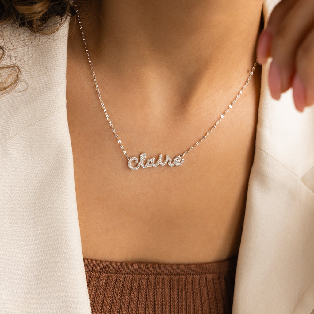 A woman wears the Pave Dream Script Name Necklace in silver, personalized with the name Claire in elegant cursive letters.
